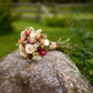 A small dried flower bouquet with cream, pink, and burgundy strawflowers resting on a large mossy rock in an outdoor garden setting.